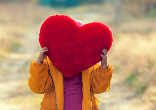Little girl hiding behind heart shaped pillow and holding it in